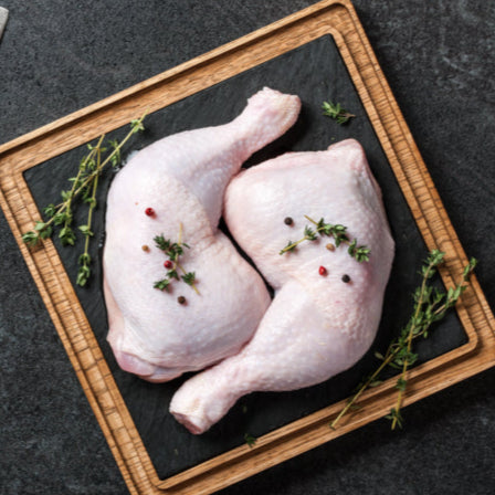 chicken leg quarters on a cutting board with a cleaver on a dark surface